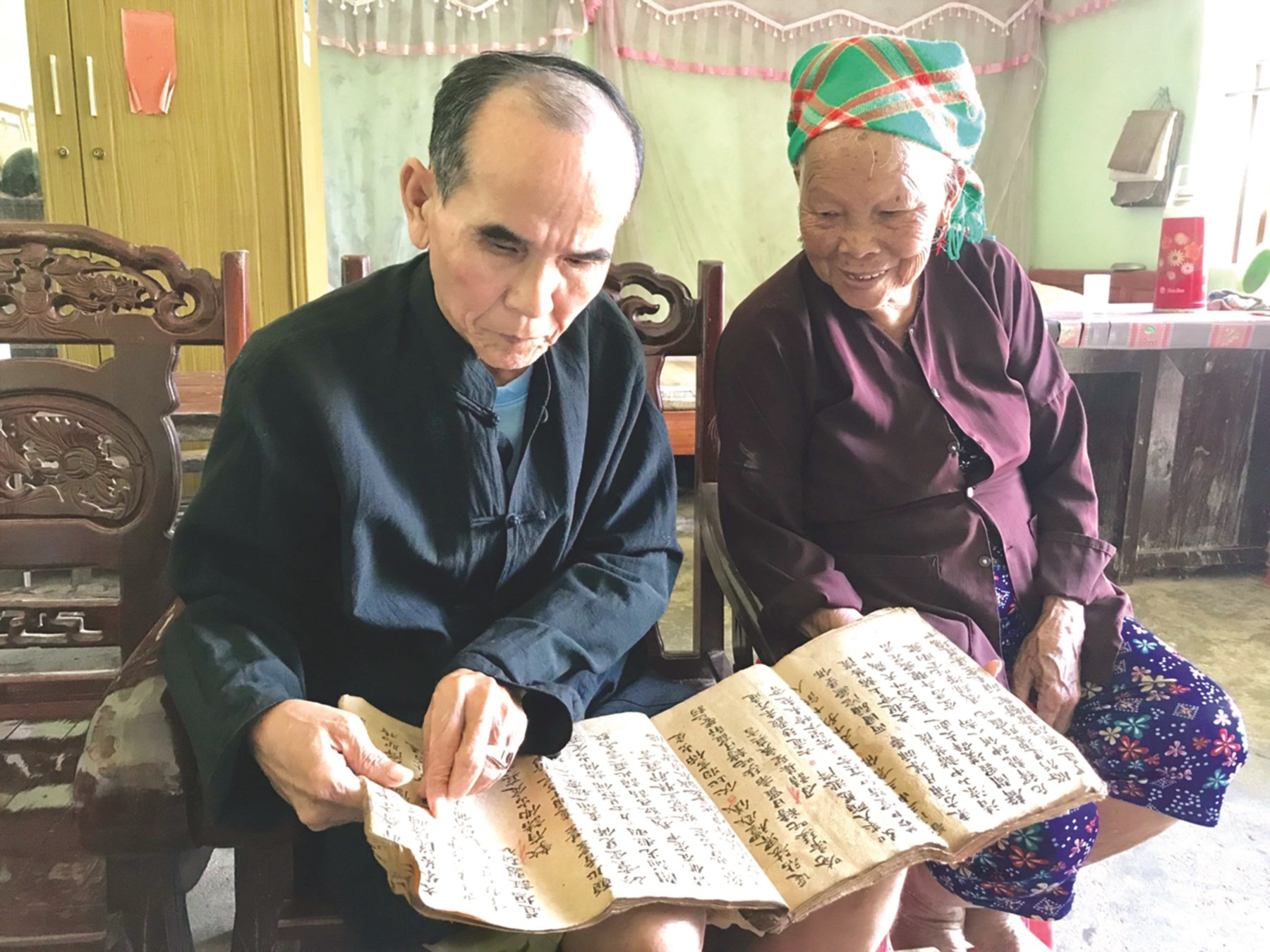 Ông Lỷ A Sáng (trái) đang nghiên cứu tài liệu cổ của người Sán Chỉ (Ảnh Ngô Dịu)