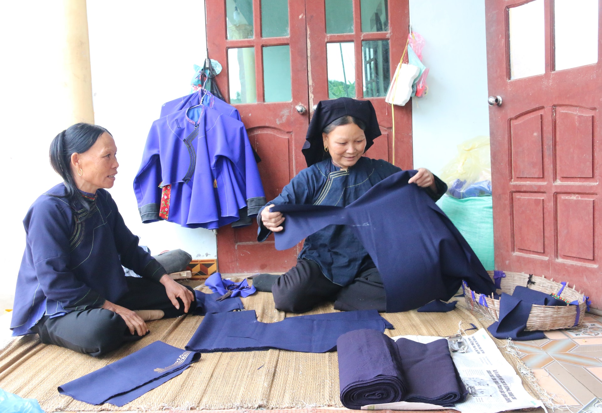 Bà Lăng Thị Liên (bên phải) đang cắt may trang phục dân tộc Nùng cho bà con trong thôn