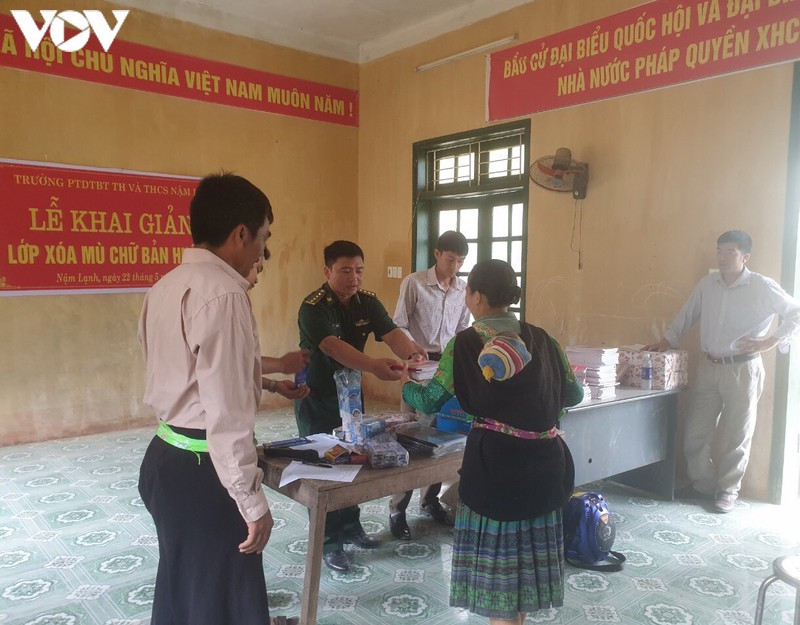 Thầy giáo quân hàm xanh ở Đồn biên phòng Nậm Lạnh (Sốp Cộp) phát sách vở, đồ dùng học tập cho học viên học lớp xóa mù chữ.