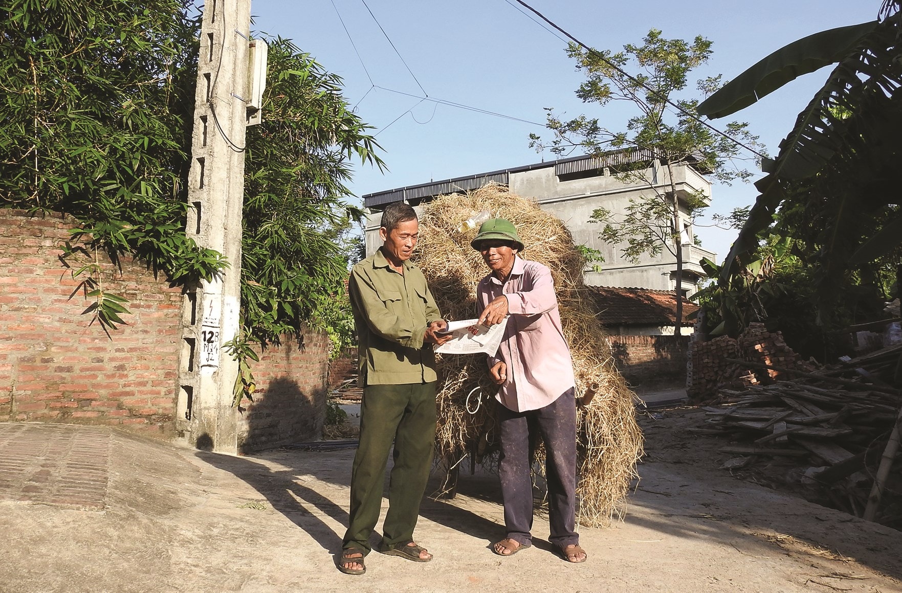 Ông Bằng Văn Ngọc (bên trái) chia sẻ thông tin trên Báo Dân tộc và Phát triển  với người dân trong thôn