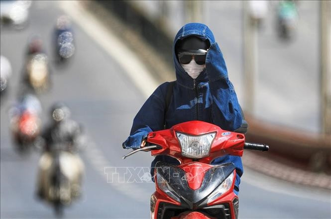  Người dân trang bị khẩu trang, áo chống nắng kín mít vẫn phải giơ tay che mặt vì nắng nóng cộng với tỉ lệ tia cực tím cao. Ảnh: Thành Đạt/TTXVN