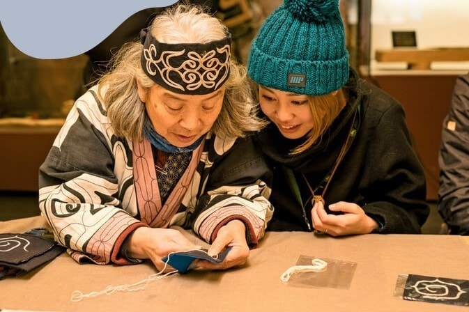 Người Ainu (bên trái) giới thiệu về nghề thêu thủ công truyền thống tại Bảo tàng Akanko Ainu Kotan