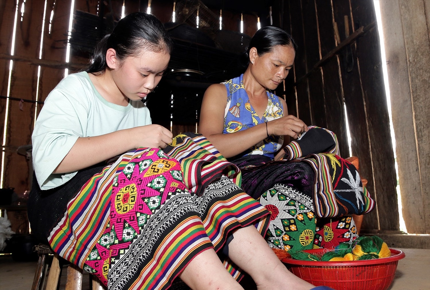Trong những ngày nghỉ Hè, các em học sinh người Thái ở nhà cùng mẹ thêu hoa văn trên chân váy để kiếm tiền mua sách vở cho năm học mới