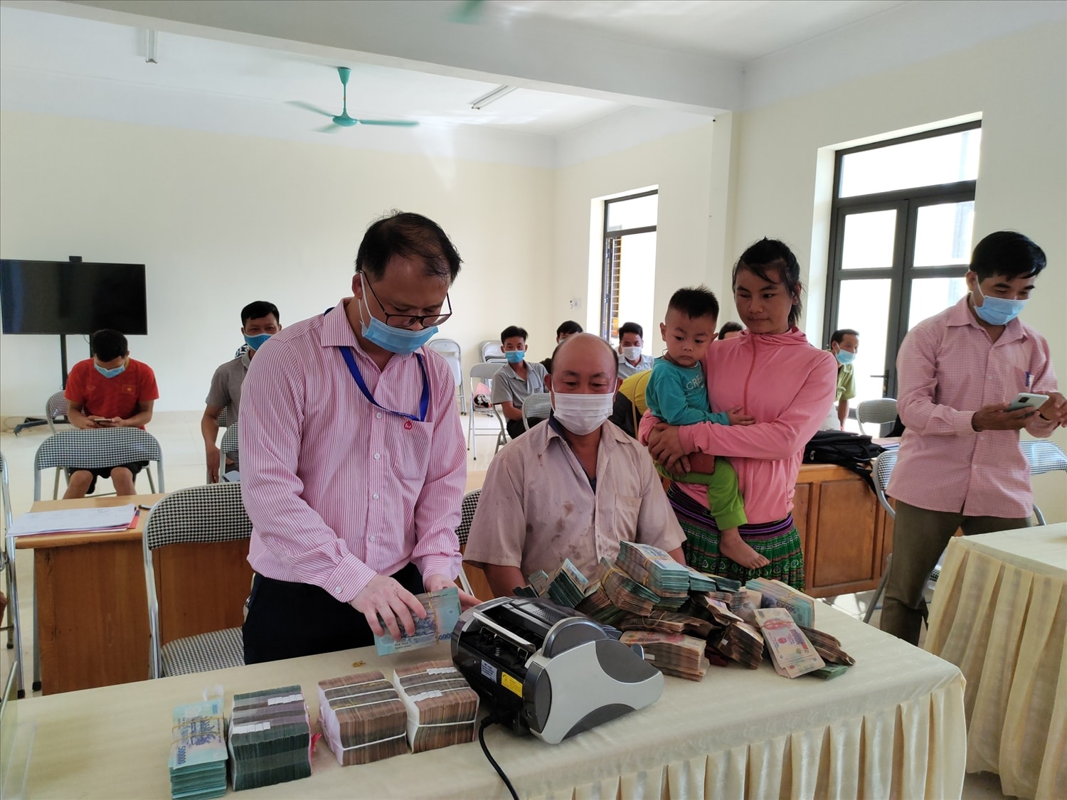 Cán bộ Phòng giao dịch NHCSXH huyện Văn Chấn giúp vợ chồng anh Giàng A Sáu xếp gọn tiền trước khi gửi tiết kiệm.