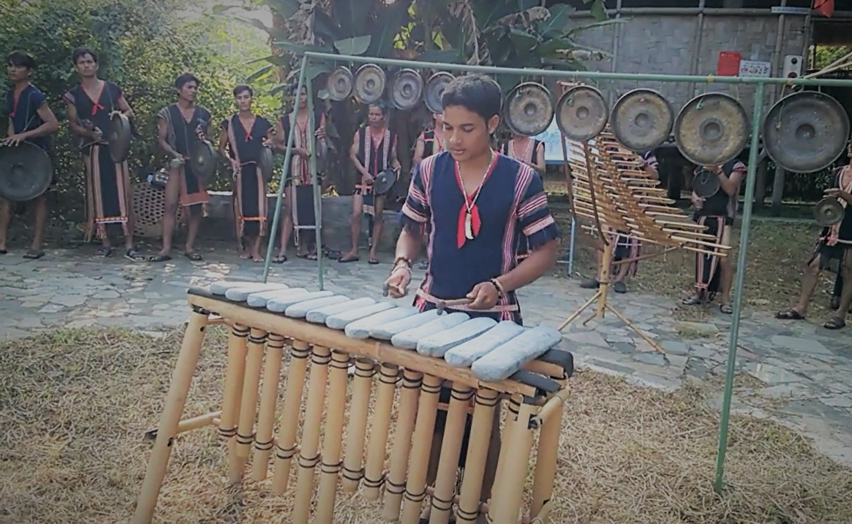 Nghệ nhân chơi đàn đá Kaly Trần (người Ba Na) cùng dàn cồng chiêng Tây Nguyên.