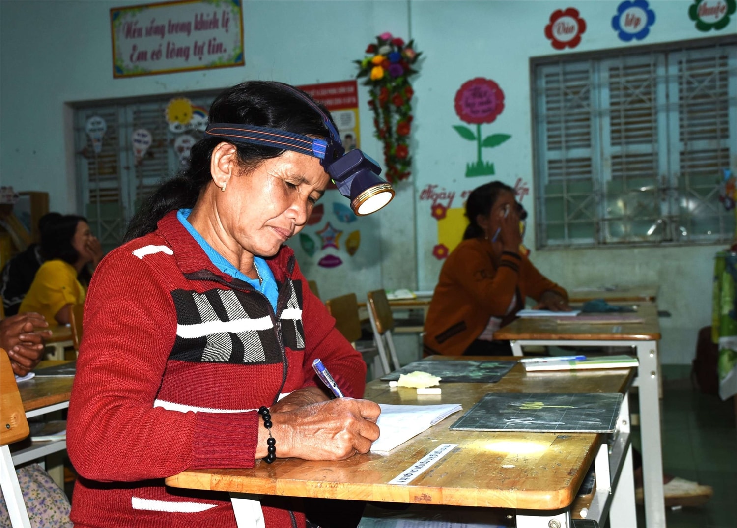 Đôi mắt không còn sáng nên bà Y Êh đội đèn pin trên đầu để học tập