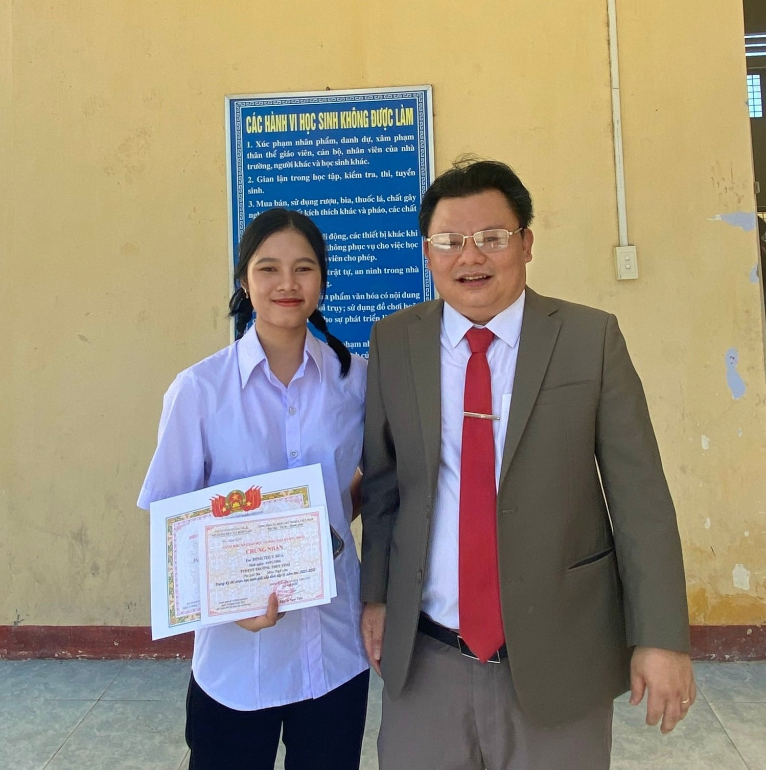 Đinh Thị Y Dua chụp hình cùng thầy Hiệu trưởng trong một lần được vinh danh các học sinh đạt giải cao trong các kỳ thi