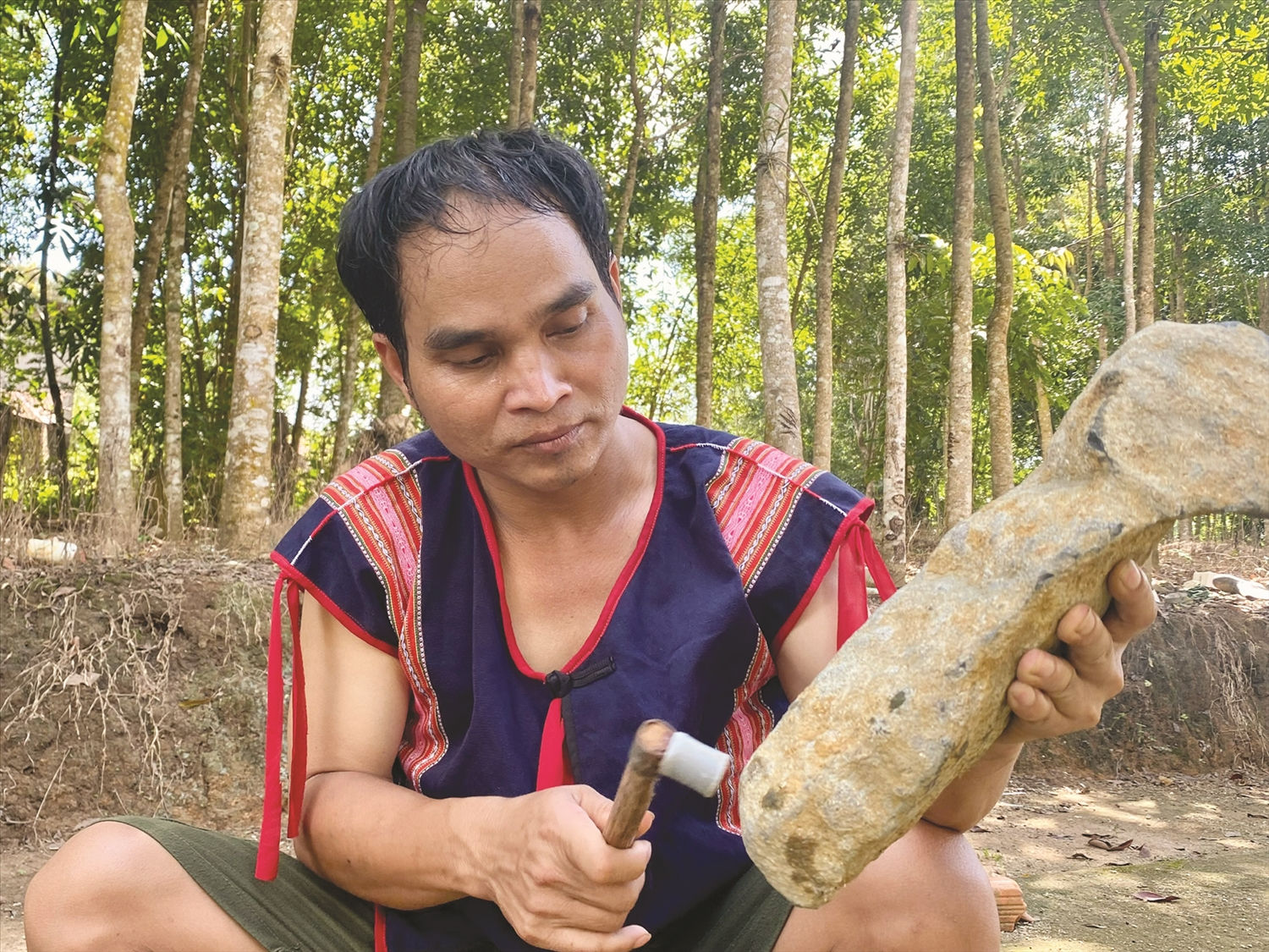 Nghệ nhân Ưu tú A Huynh cẩn thận gọt các thanh đá để chỉnh âm  cho giàn đàn đá.