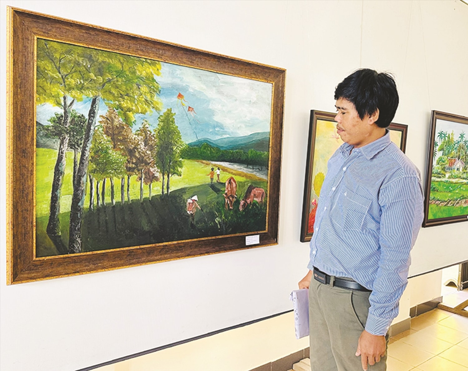 Họa sĩ KPă Tý bên tác phẩm “Hương quê tôi” tại Triển lãm ở Hội VHNT tỉnh Phú Yên tháng 12/2023. Ảnh: Nhân vật cung cấp.