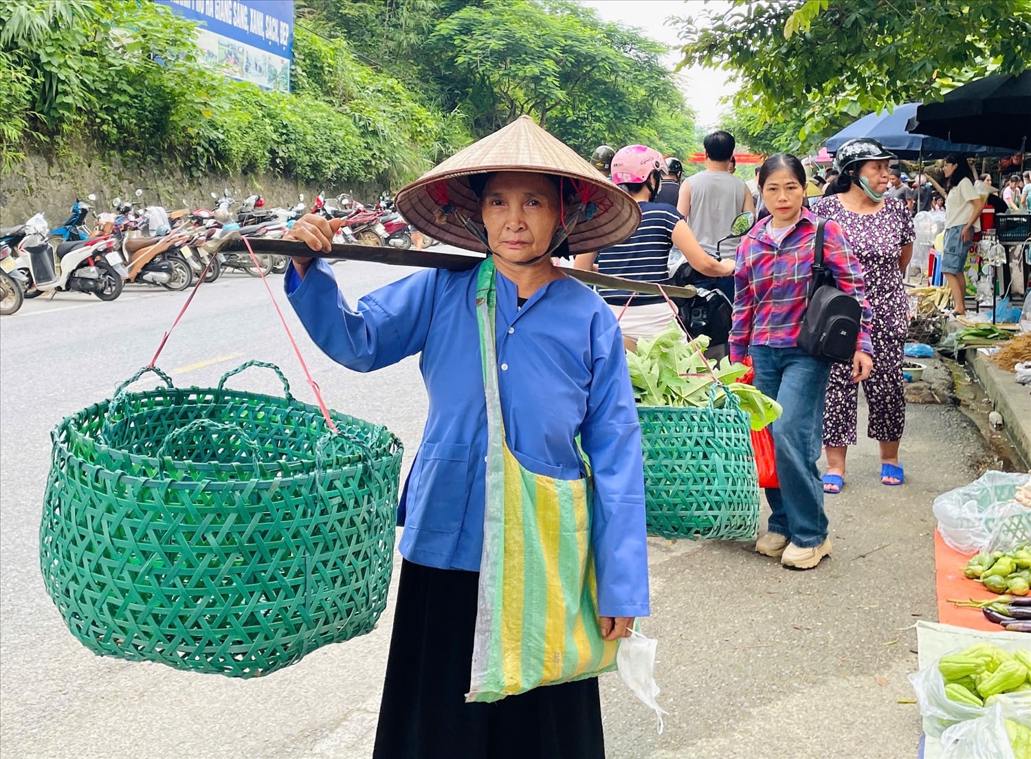 Bà cụ gánh những chiếc làn nhựa do chính tay mình đan, chậm rãi bước vào chợ phiên - hình ảnh thân quen và đầy chất quê giữa núi rừng.