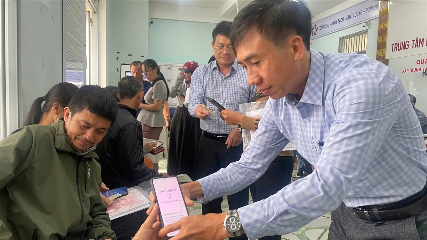 Cán bộ Trung tâm phục vụ hành chính công xã Đăk Hà hướng dẫn người dân cài đặt ứng dụng đặt lịch trực tuyến UniQMS. (Ảnh: Ngọc Chí)