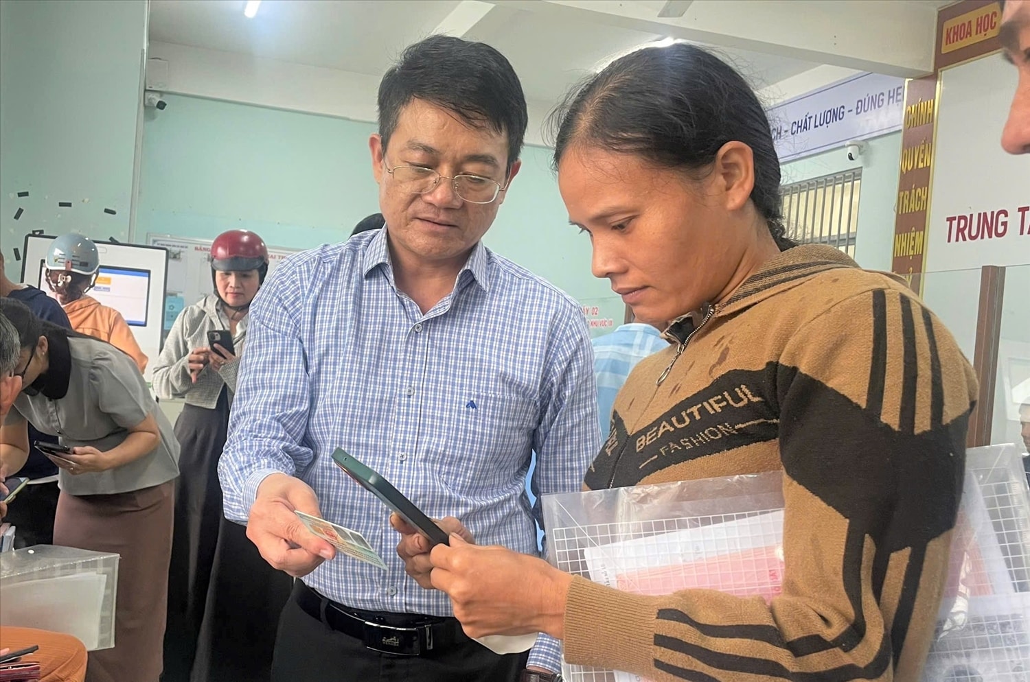 Ông Nguyễn Minh Vương (bên trái), Chủ tịch UBND xã Đăk Hà hướng dẫn người dân cách cài đặt và sử dụng ứng dụng đặt lịch trực tuyến UniQMS. (Ảnh: Ngọc Chí)