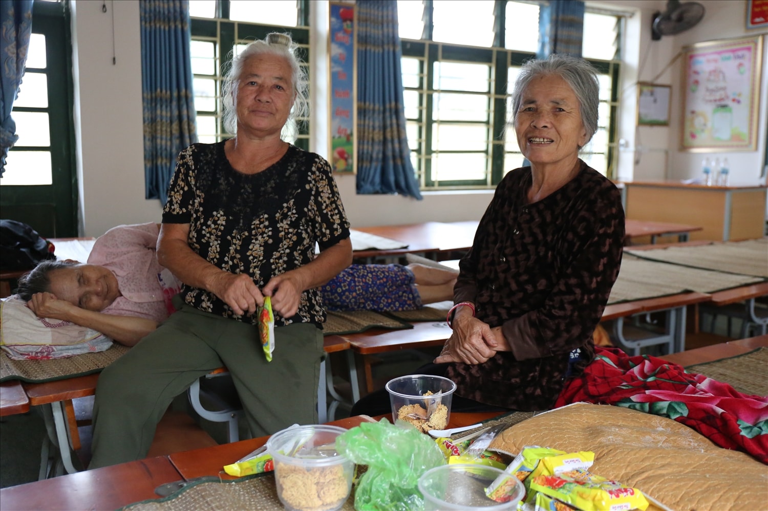 Bà Nguyễn Thị Nhung (70 tuổi), bìa trái và bà Bùi Thị Đoàn (71 tuổi), ở xóm Bắc Chiến Thắng chuẩn bị cho bữa ăn tạm tại nơi tránh trú bão - Ảnh: Thanh Hải