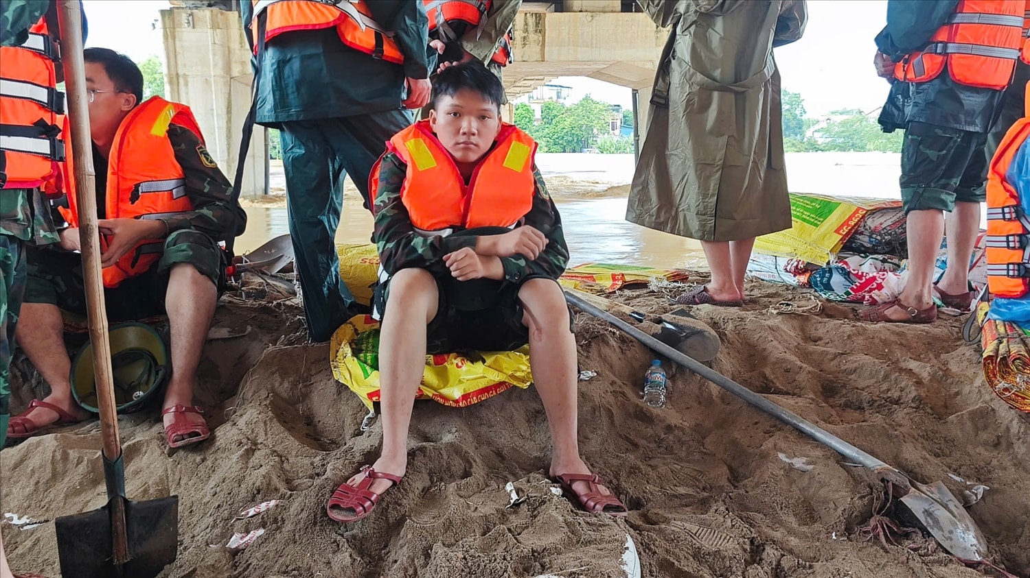 Sau nhiều giờ dầm mình trong nước, lực lượng hộ đê tranh thủ nghỉ ngơi ngay bên bờ đê để lấy sức tiếp tục nâng cao bờ đê thêm khoảng 50cm trước 14 giờ chiều nay. (Ảnh: Nguyễn Liên)
