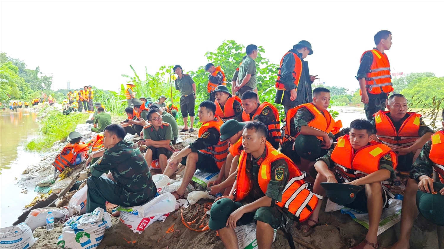 Sau nhiều giờ dầm mình trong nước, lực lượng hộ đê tranh thủ nghỉ ngơi ngay bên bờ đê để lấy sức tiếp tục nâng cao bờ đê thêm khoảng 50cm trước 14 giờ chiều nay. (Ảnh: Nguyễn Liên)