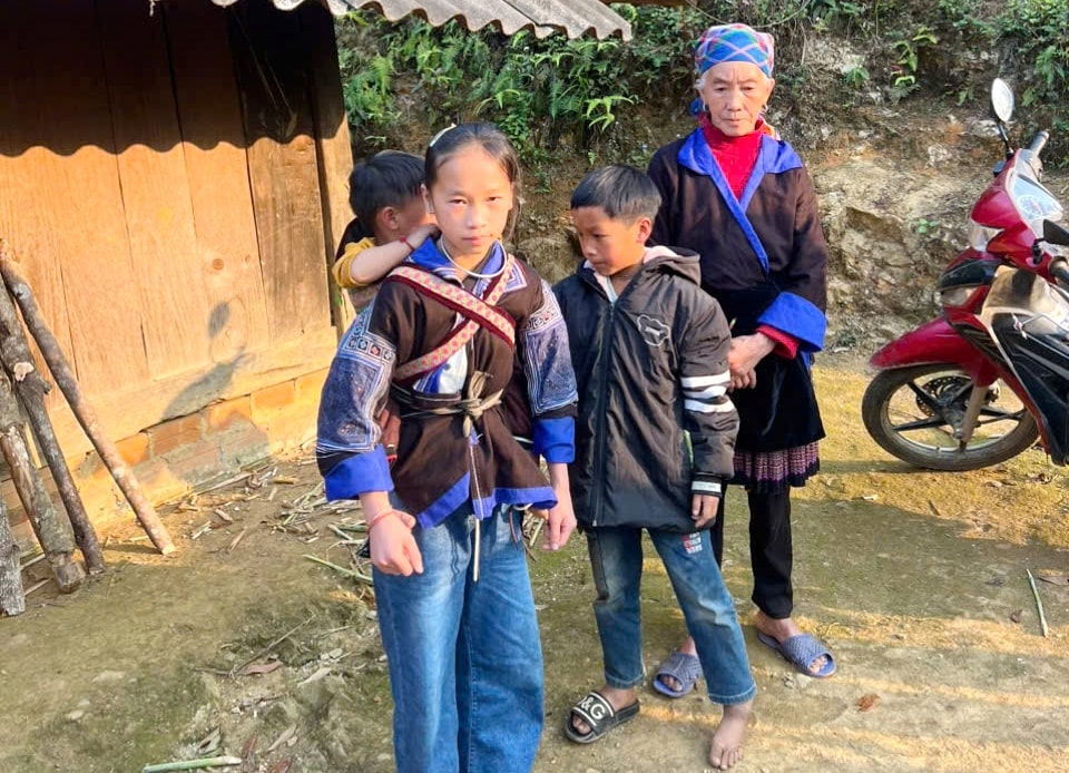 Cụ Mùa Thị Dở gầy guộc cùng ba cháu nhỏ đứng trước ngôi nhà gỗ tuềnh toàng,  nơi bão tố cuộc đời vừa ập xuống