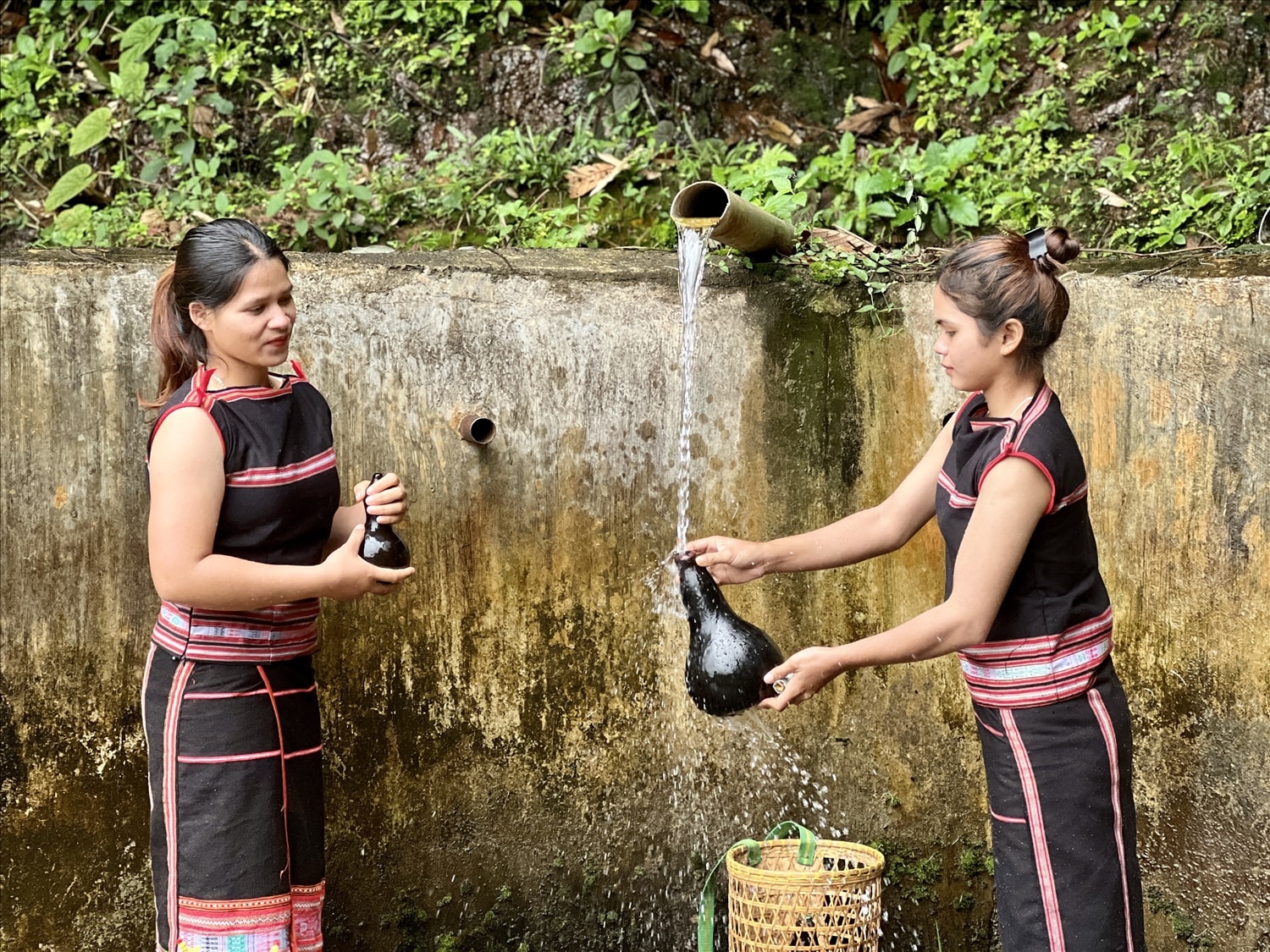 Phụ nữ Gia Rai dùng quả bầu khô lấy nước bên giọt nước truyền thống của làng