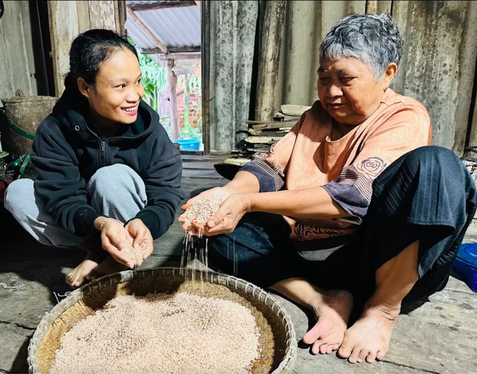 Bà Đoàn Thị Hồng (bên phải) sàng những hạt gạo có màu đỏ thẫm (giống lúa Đá Đỏ), đã nuôi sống bao thế hệ người Chăm Hroi. (Ảnh: D.Đ)