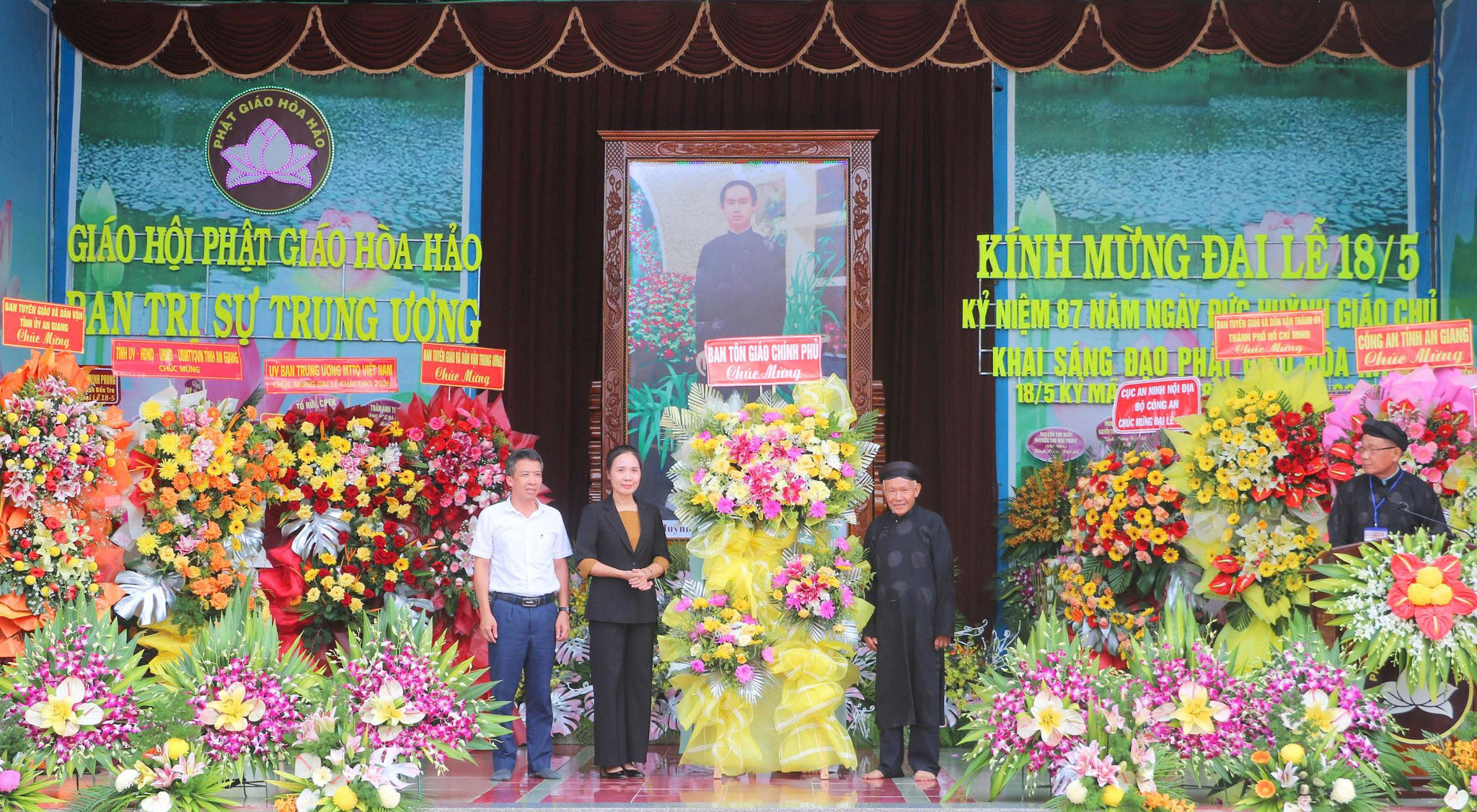 Bà Trần Thị Minh Nga, Phó Trưởng Ban Tôn giáo Chính phủ - Bộ Dân tộc và Tôn giáo (trái) tặng hoa, chúc mừng Đại lễ kỷ niệm 87 năm Ngày khai sáng đạo Phật giáo Hòa Hảo